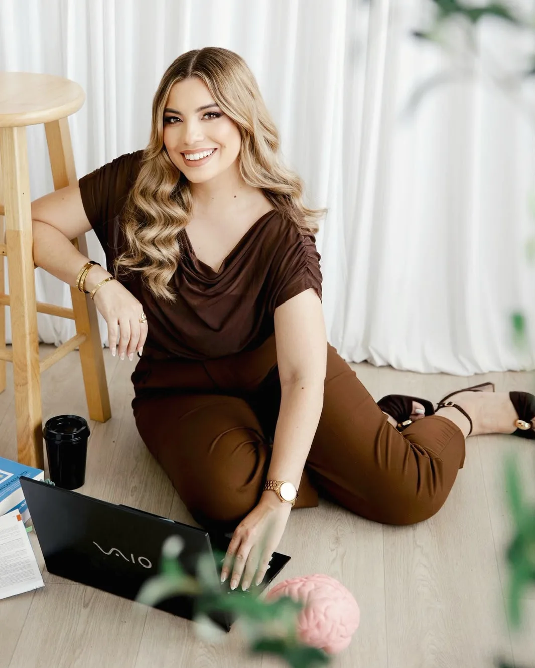 Melanie trabaja en su laptop, sentada en el piso junto a un banquillo y libros de psicología