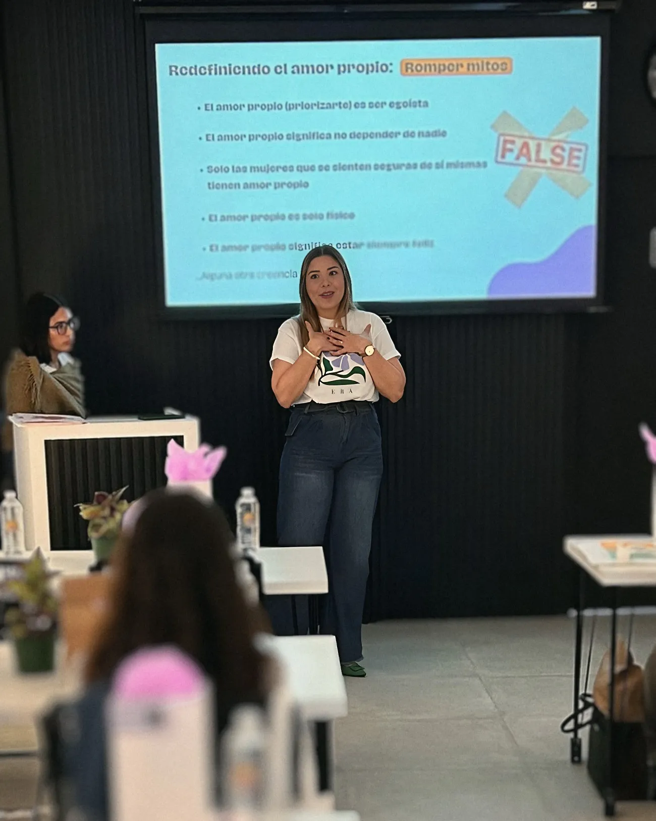 Vista desde el público: Melanie presenta un taller sobre amor propio frente a una pantalla