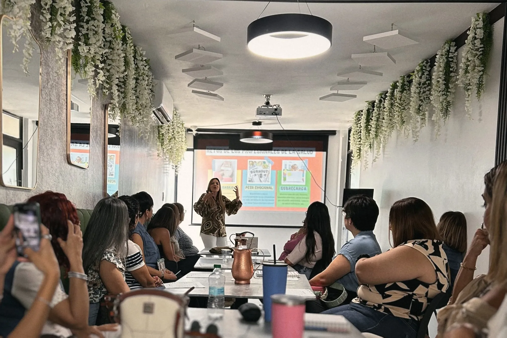 Un grupo de profesionales sentadas a una mesa larga escucha a Melanie al fondo de la sala