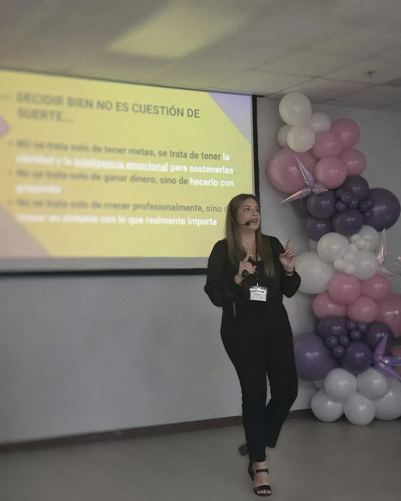 Melanie, con micrófono de diadema, da una charla junto a una pantalla con el título “Decidir bien no es cuestión de suerte”